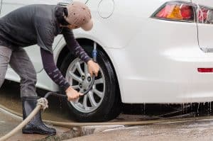 Car washing.A man cleaning wheels using high pressure water jet at car wash station.
